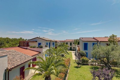 View over resort villas with gardens, palm trees, and tiled roofs.
