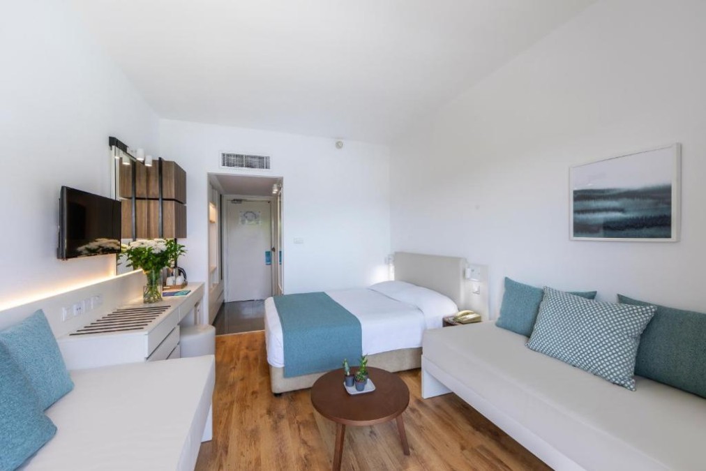 Bright guest room with bed, sofa, round table and desk area.
