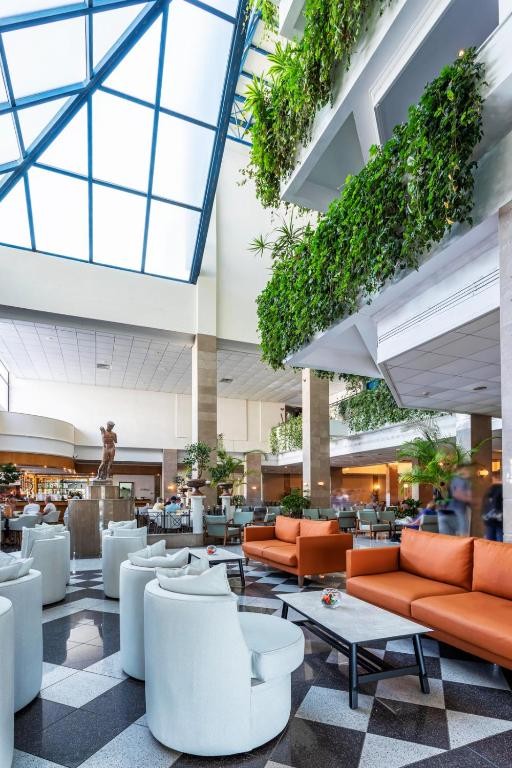 Hotel atrium lounge with seating areas, plants and glass roof.