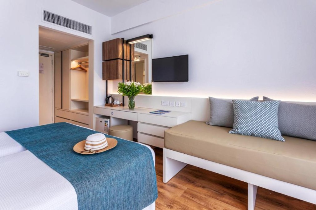Modern guest room with bed, sofa, desk, TV and open wardrobe.