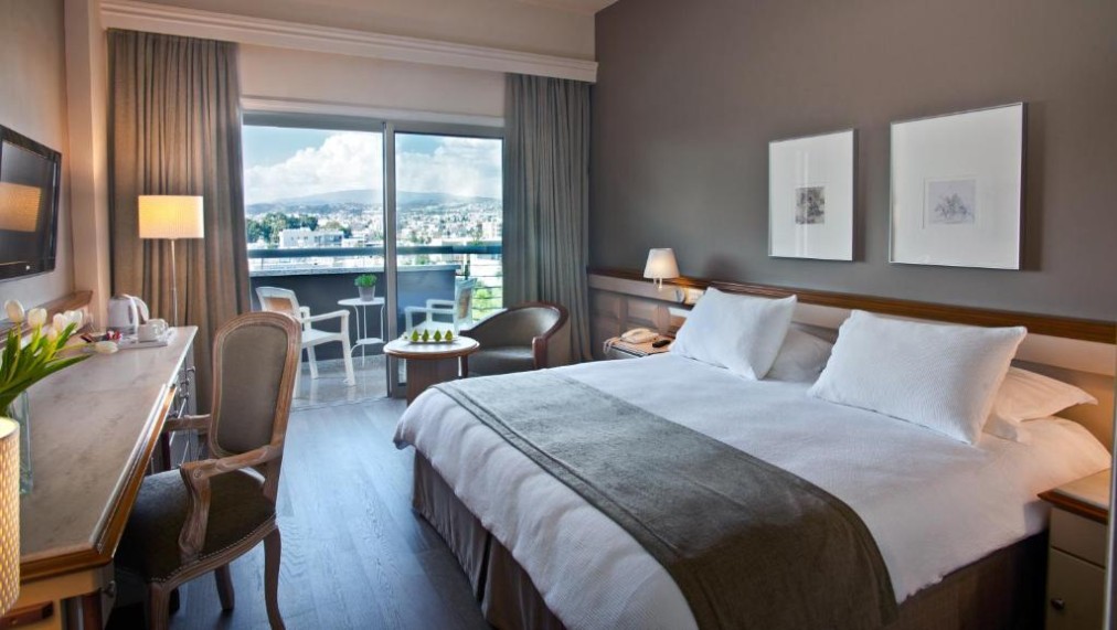 Guest room with double bed, desk and balcony overlooking the city.