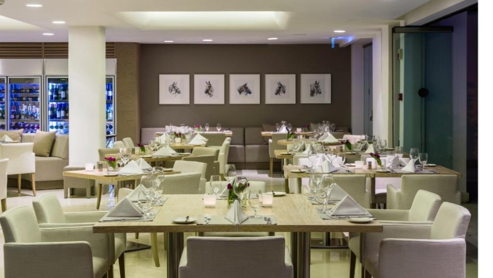 Restaurant dining room with set tables, upholstered chairs and framed wall art.