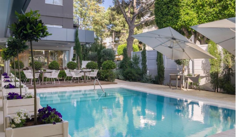 Outdoor pool with surrounding deck, umbrellas and garden seating.