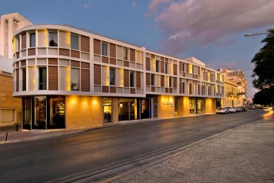 Modern hotel exterior on a city street at dusk with illuminated facade and entrance.