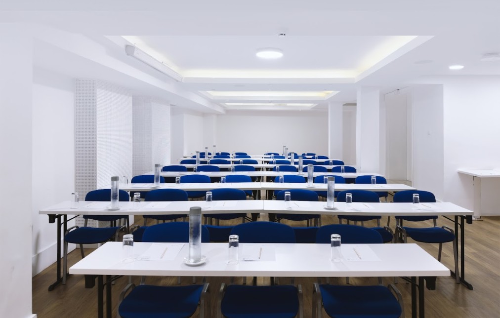 Conference room with classroom-style tables, blue chairs, water bottles and notepads.