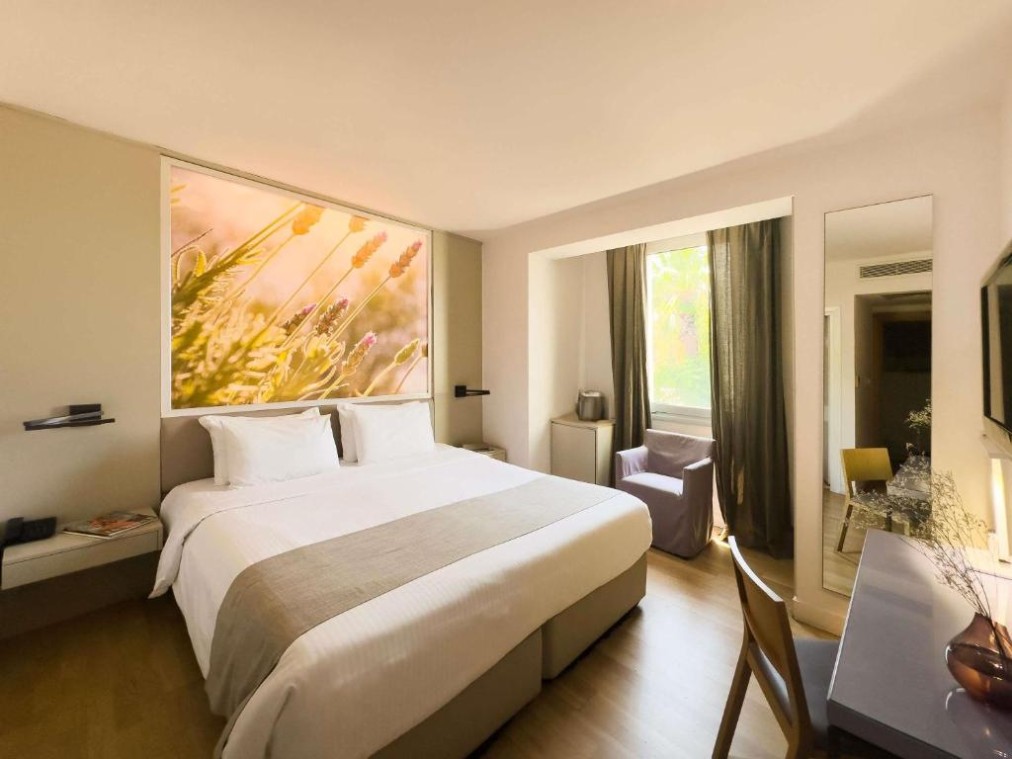 Guest room with double bed, desk, armchair and large botanical artwork above the headboard.