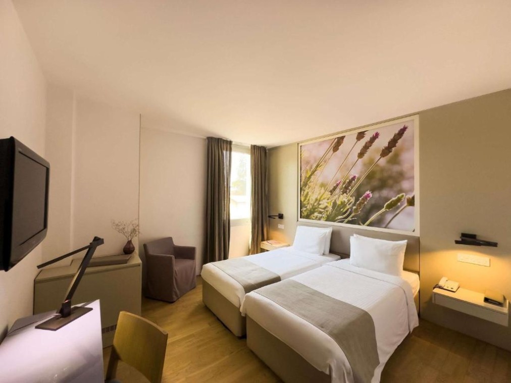 Twin guest room with desk, TV, armchair and large floral artwork behind the beds.