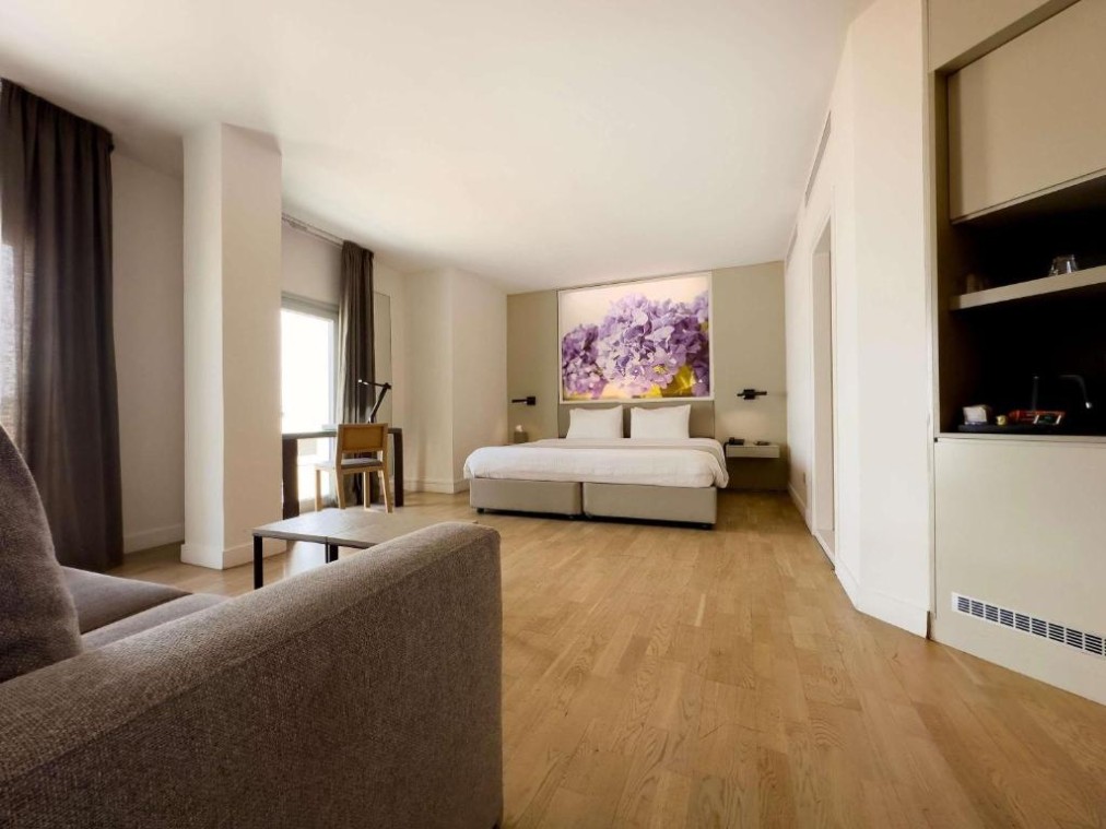 Spacious suite-style room with double bed, sofa, table and wood flooring.
