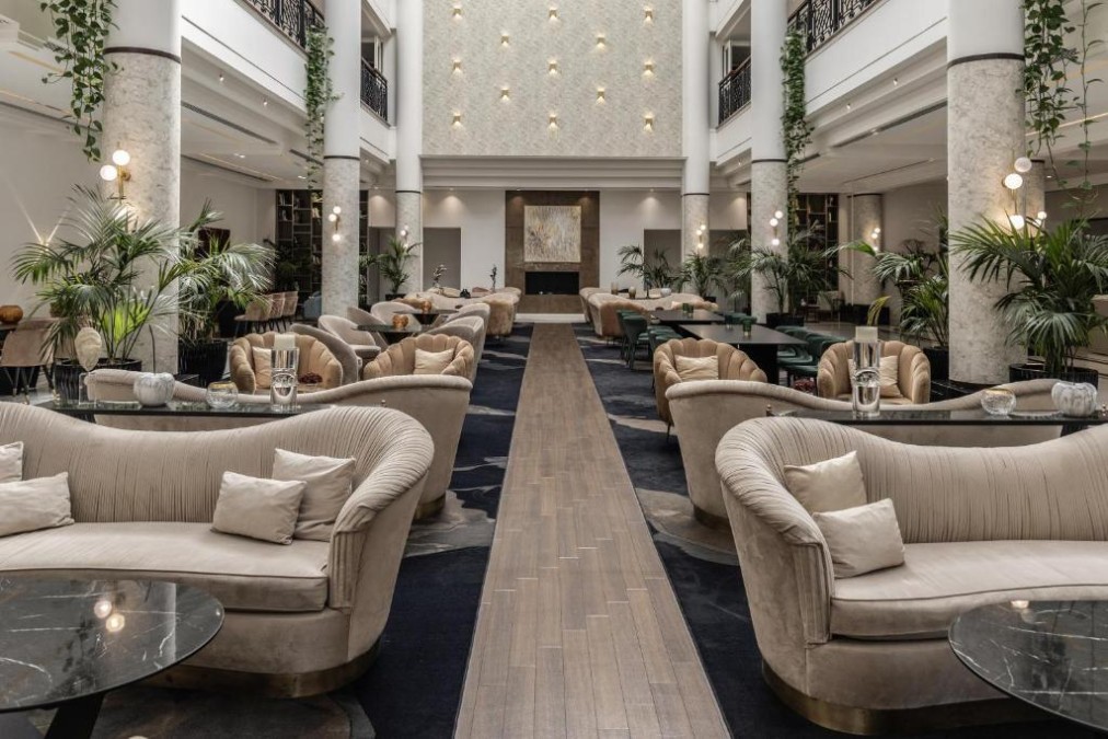 Hotel lobby lounge with sofas, marble columns and central fireplace.