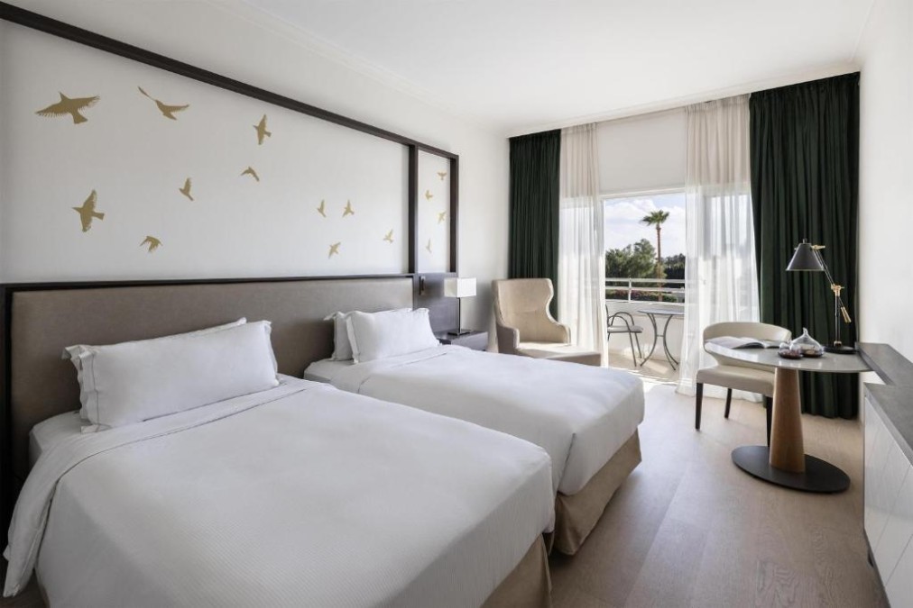 Twin guest room with balcony seating, desk and garden view.