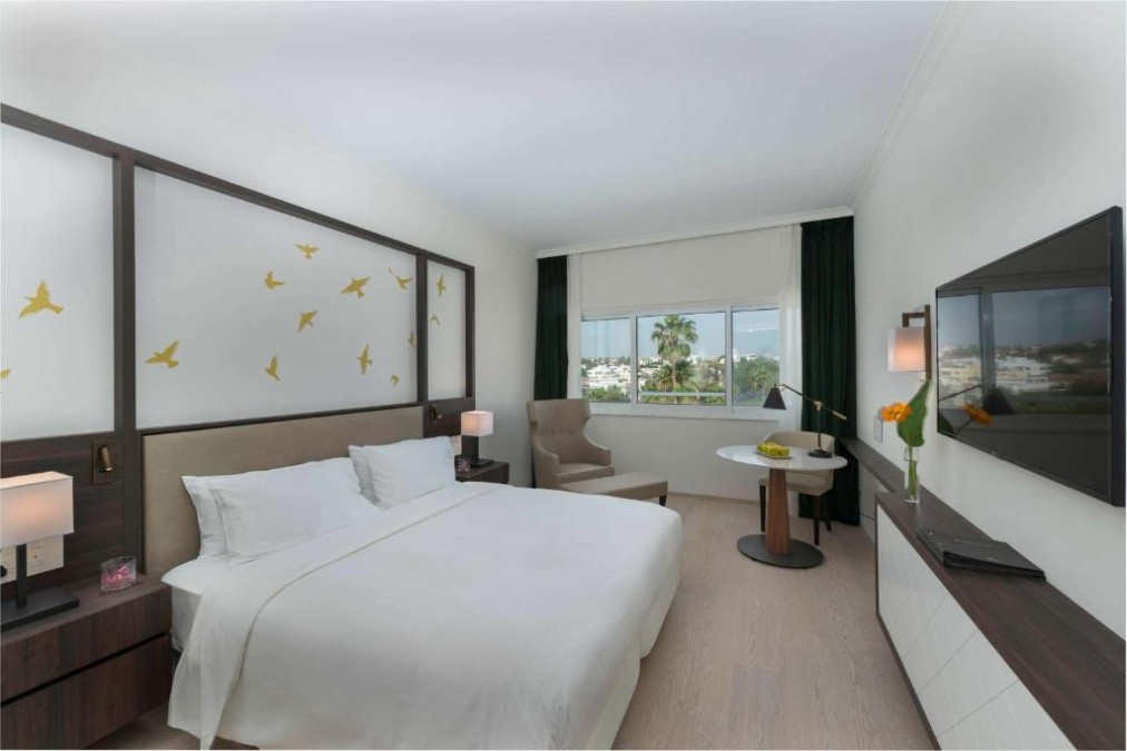 King guest room with wall-mounted TV, table and city view.