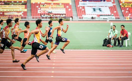 Sprinters accelerating from the start on a red track inside a stadium, athletes competing in a training camp practice session
