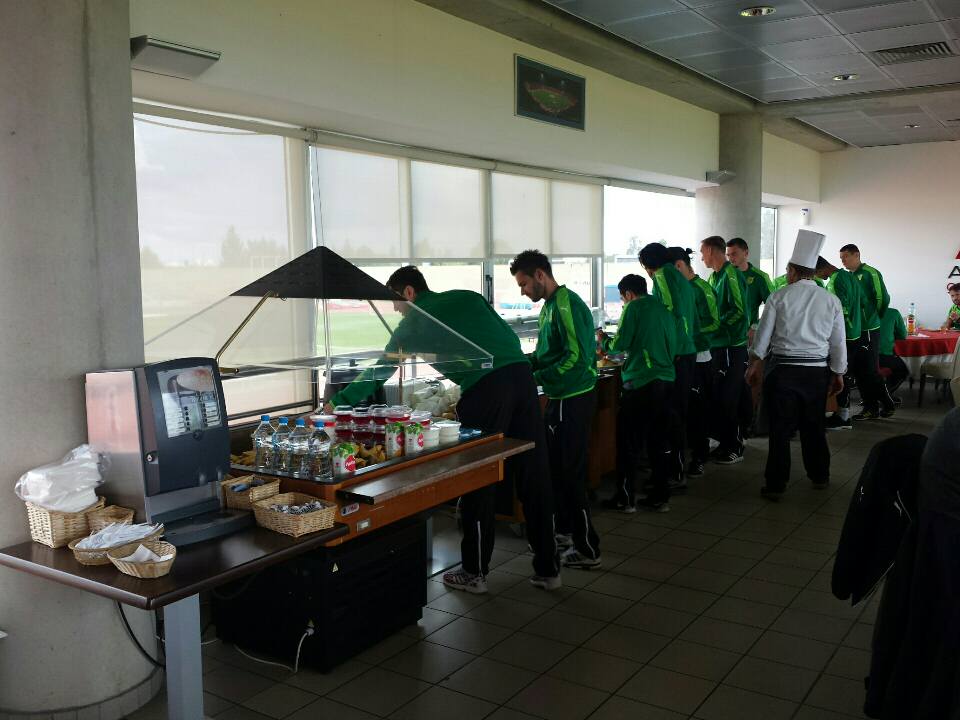 Athletes in green sportswear selecting meals from buffet during training camp dining