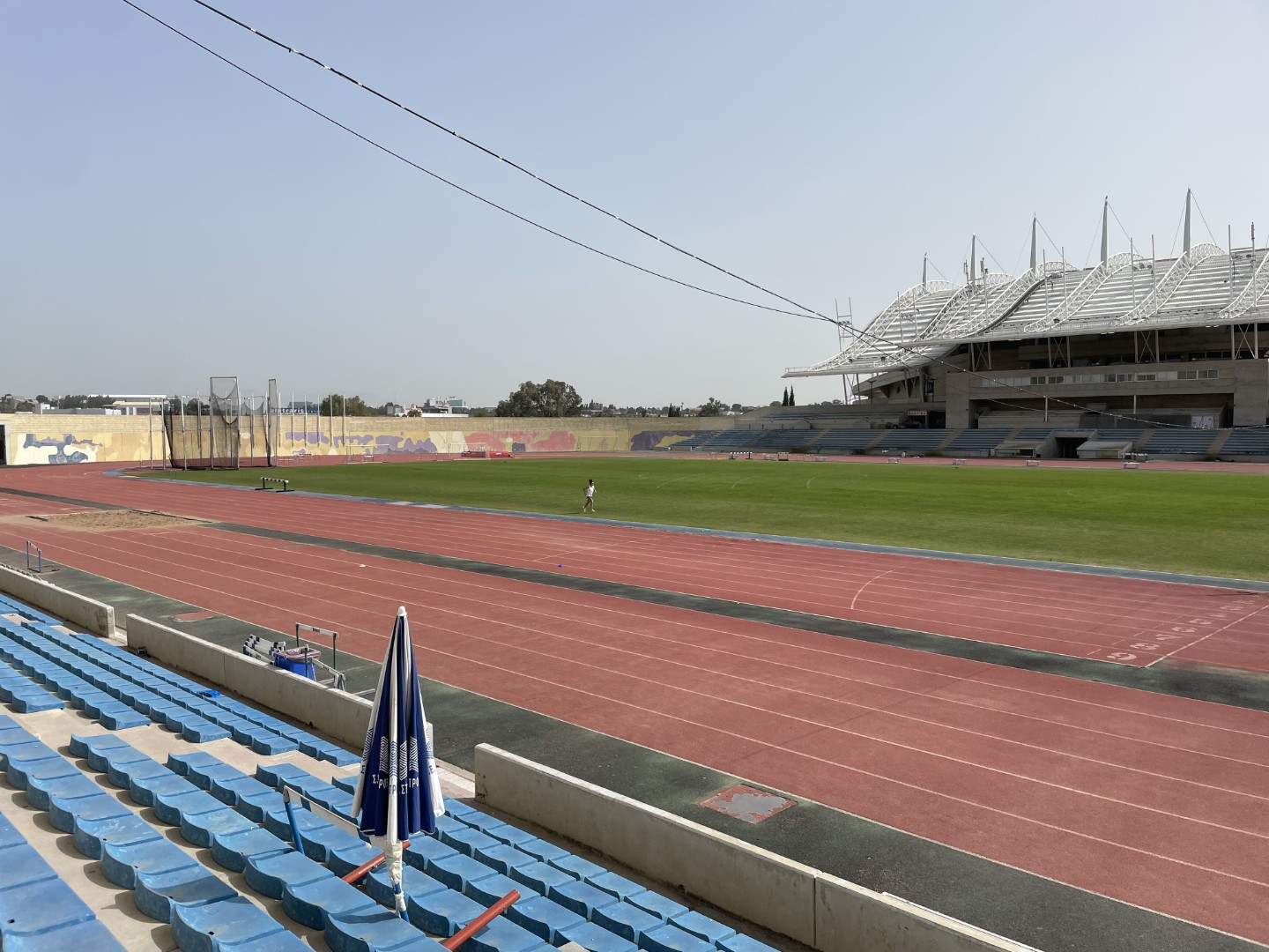 Athletics stadium with red running track, green field, and modern grandstand used for training camps and practice sessions