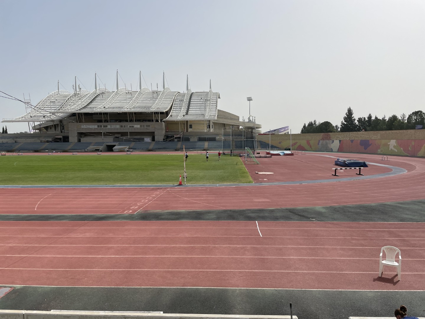 Outdoor athletics stadium with red running track, green field, and modern grandstand for training camps