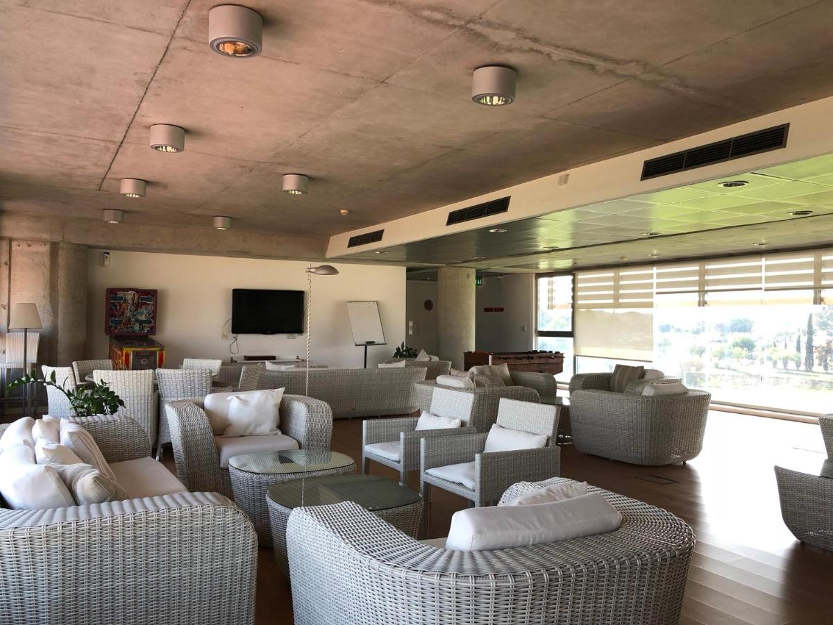 Lounge area with wicker furniture, white cushions, and large windows overlooking sports facilities