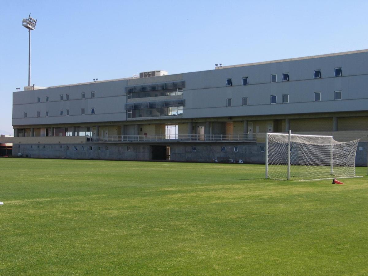 Green football training field with goalpost and modern multi-level sports building