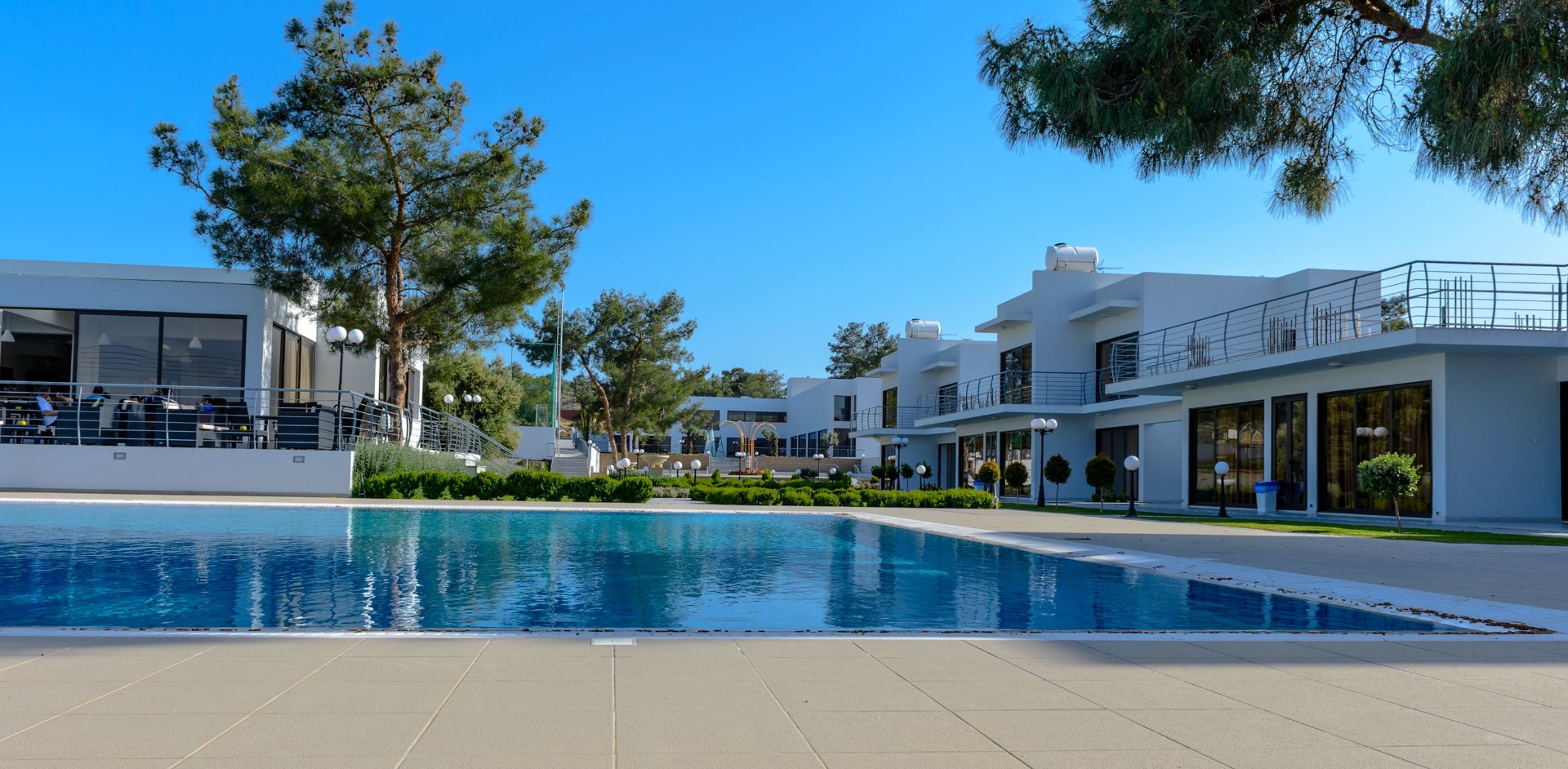Hotel complex with poolside area, white buildings, and blue sky