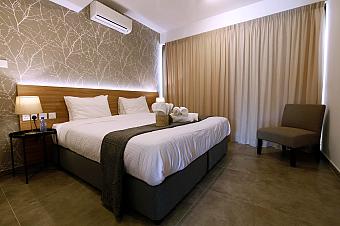 Modern hotel room with double bed, neutral decor, and soft lighting beside beige curtains