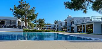 Hotel complex with poolside area, white buildings, and blue sky