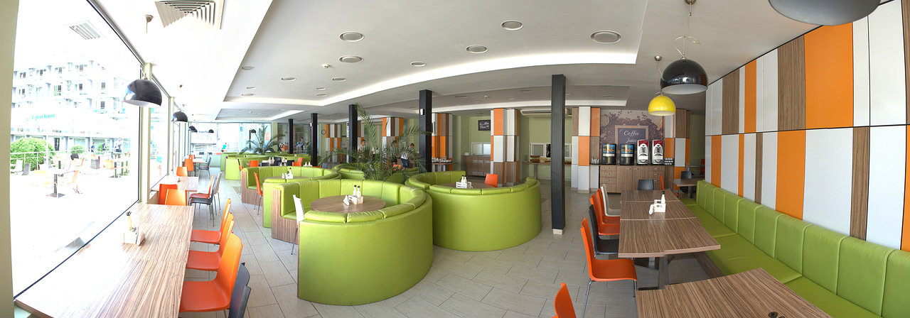 Salon moderne avec sièges verts, touches orange et tables, espace de détente pendant les temps libres du stage d'entraînement