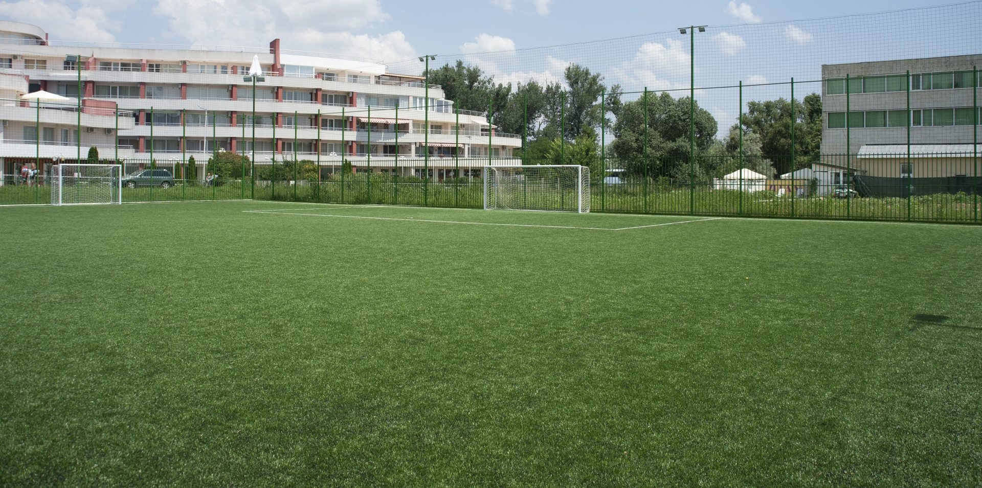 Terrain de football synthétique vert avec buts près des bâtiments, utilisé pour les exercices du stage d'entraînement