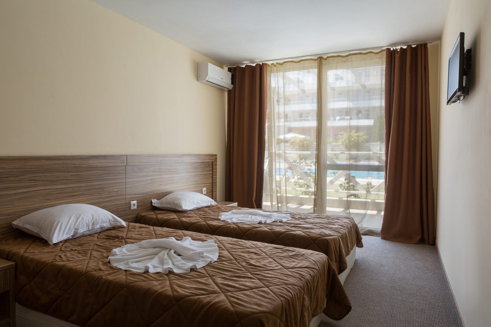 Chambre d'hôtel avec lits jumeaux, literie marron et vue sur balcon, hébergement pour athlètes en stage d'entraînement