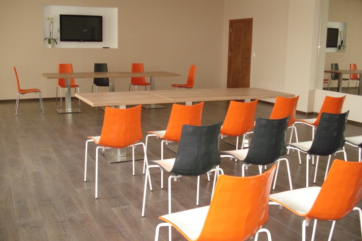 Salle de conférence avec chaises orange et noires face à un écran, disposée pour les présentations du stage d'entraînement