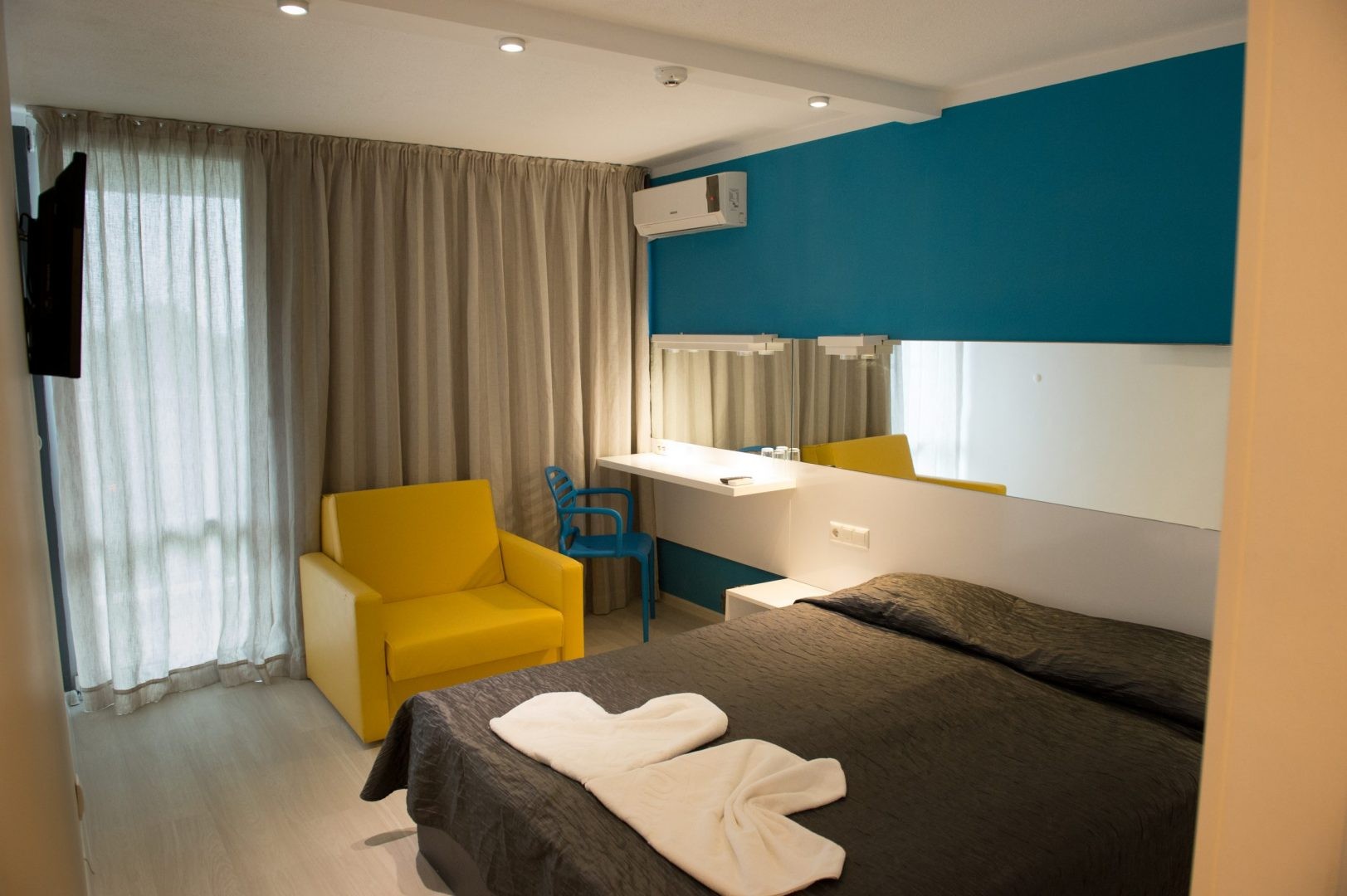 Chambre d'hôtel moderne avec couvre-lit foncé, chaise jaune et bureau, hébergement d'athlète pendant le stage d'entraînement
