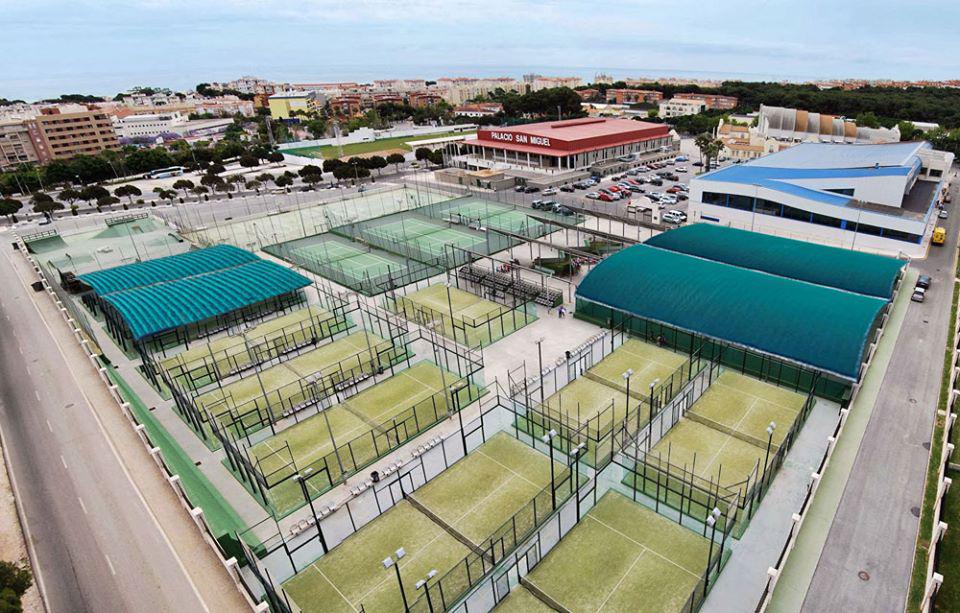 Vue aérienne de courts de padel/tennis avec sections couvertes et bâtiments adjacents.
