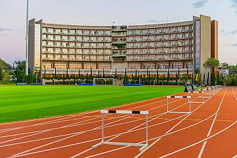 Athletics track and infield training area with hurdles set up for sprint and technique work. Stadium lighting and ample space support structured sessions for teams and individual athletes.