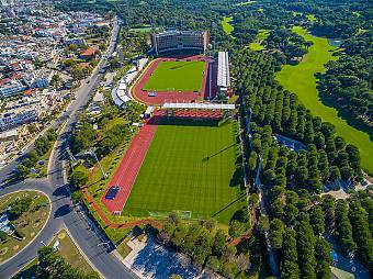 Aerial view of a large sports complex with stadium facilities and multiple training fields set within green surroundings. The layout highlights the scale and variety of venues available for camps and tournaments.