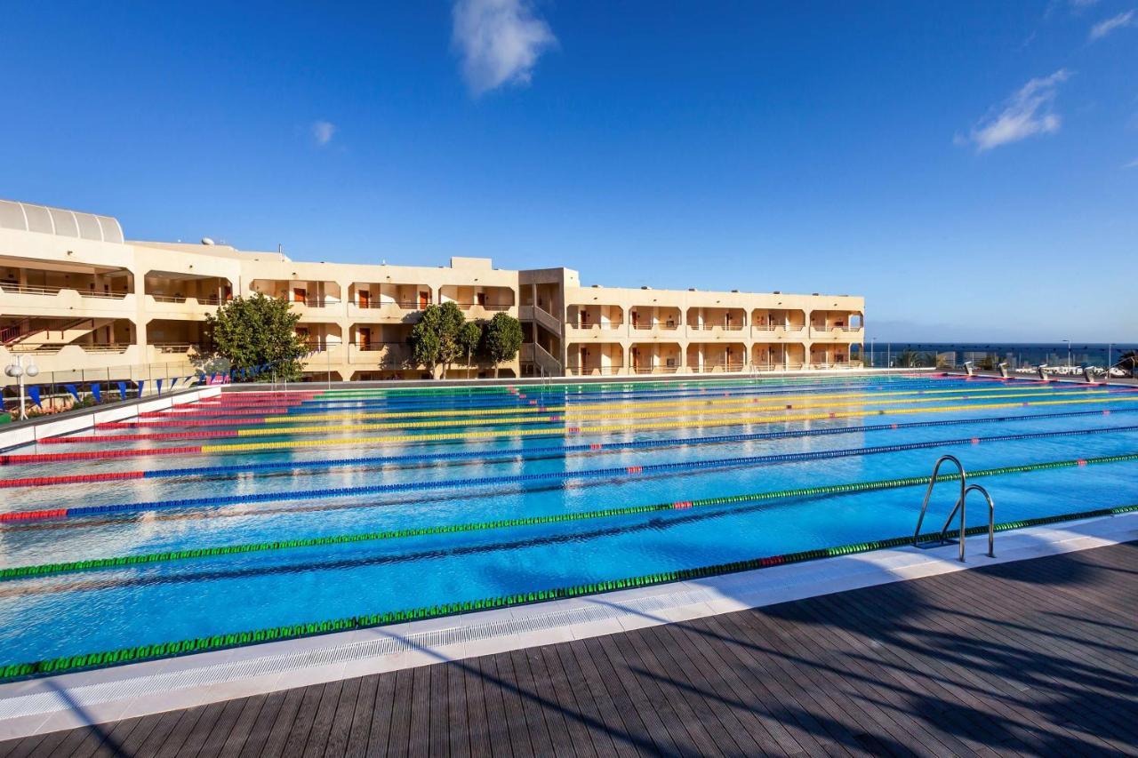 Weite Ansicht eines Außen-Schwimmbeckens neben Resortgebäuden und Meer.