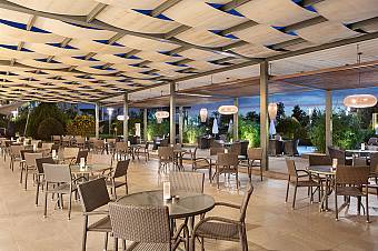 Covered outdoor terrace with tables and lounge seating in evening lighting.