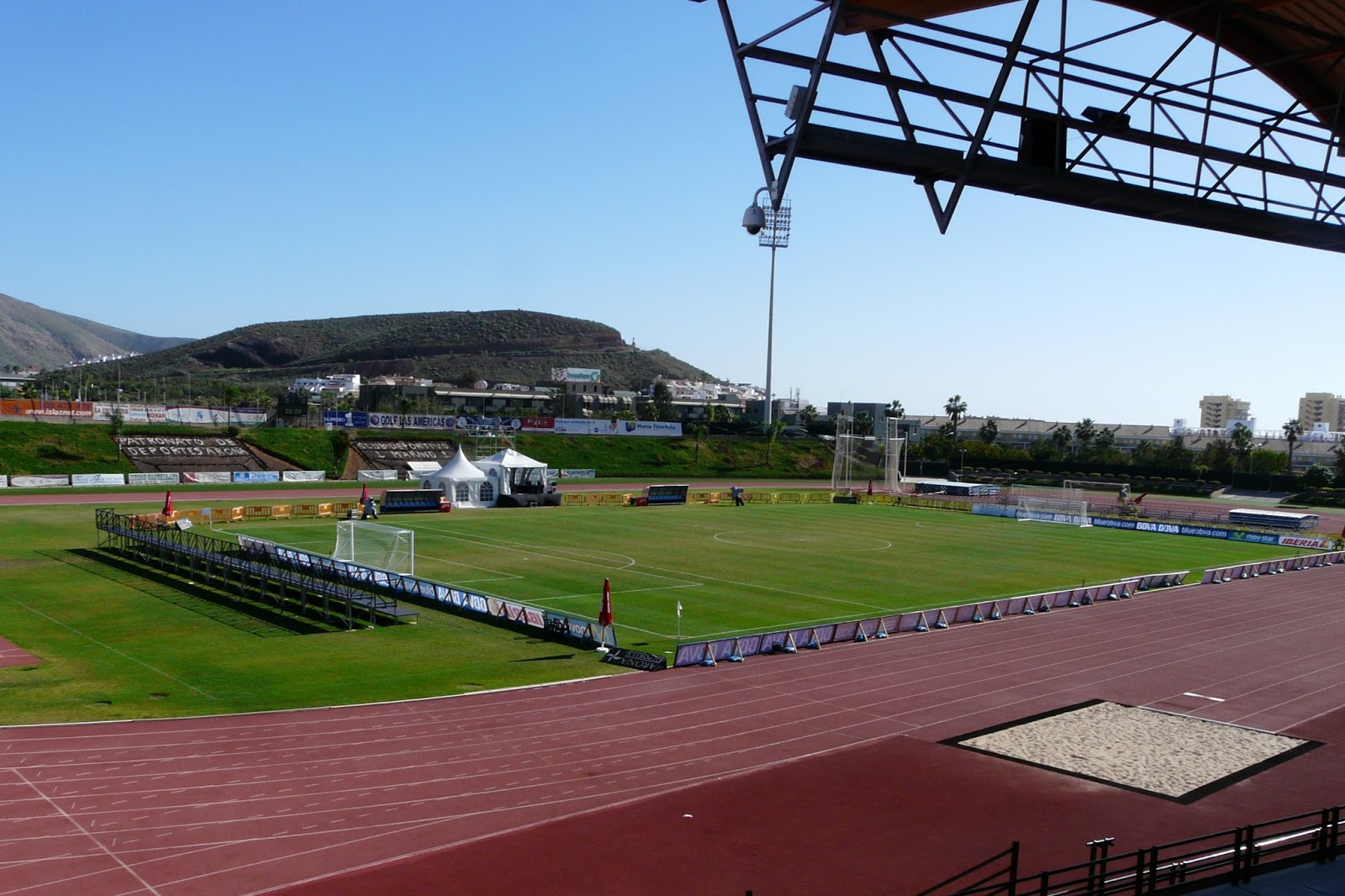 Vue depuis une tribune couverte sur un terrain de football et une piste de course dans un stade multisports.