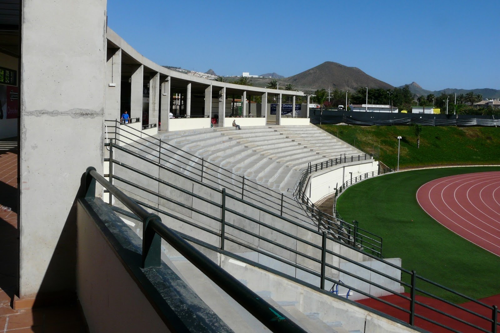 Gradins en béton à côté d'une piste d'athlétisme extérieure, avec des montagnes au loin.