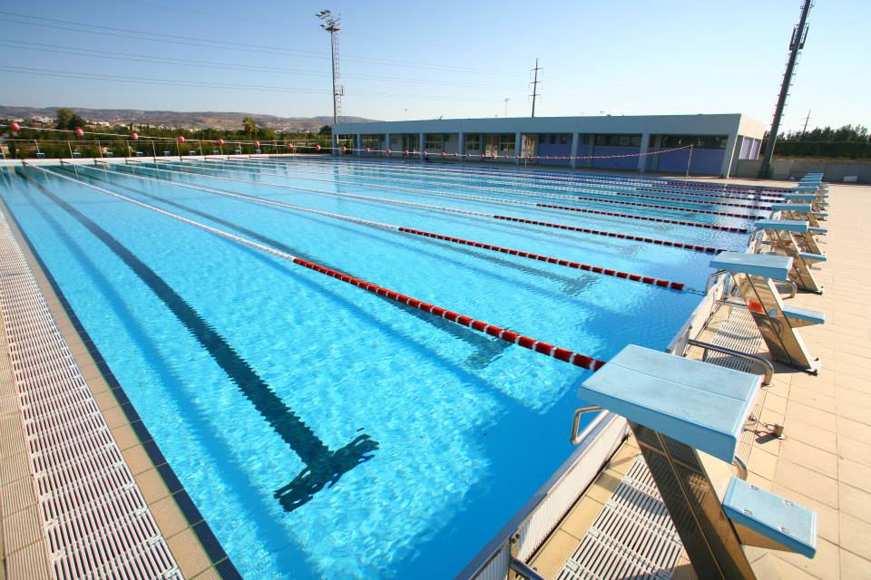 Außen-Schwimmbecken mit Startblöcken und einem Gebäude am Beckenrand.