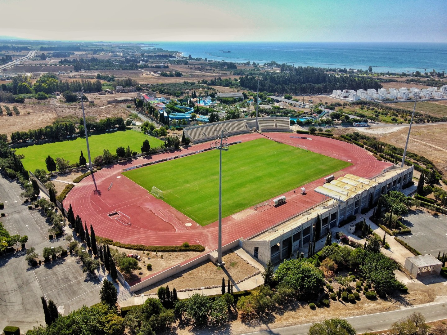 Luftaufnahme eines Stadions mit Laufbahn und Fußballfeld nahe der Küste.