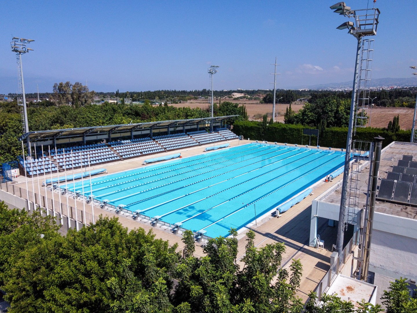 Luftaufnahme eines Außen-Schwimmbeckens mit Flutlicht und Zuschauertribüne.