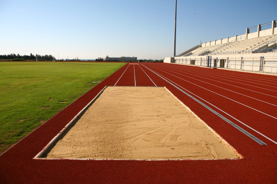 Rote Leichtathletikbahn mit Weitsprunggrube, Rasenfeld und Stadiontribüne.