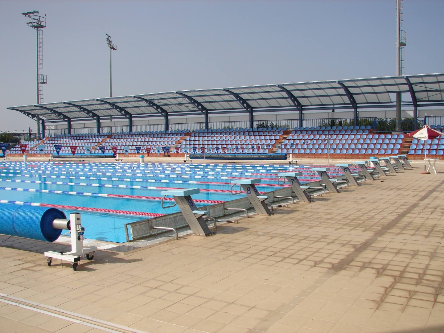 Außen-Schwimmbecken mit Startblöcken und überdachter Zuschauertribüne.