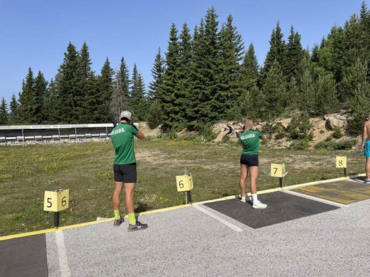 Athlètes pratiquant le tir sur cible dans un stand extérieur, couloirs numérotés aménagés parmi les arbres pendant le stage d'entraînement