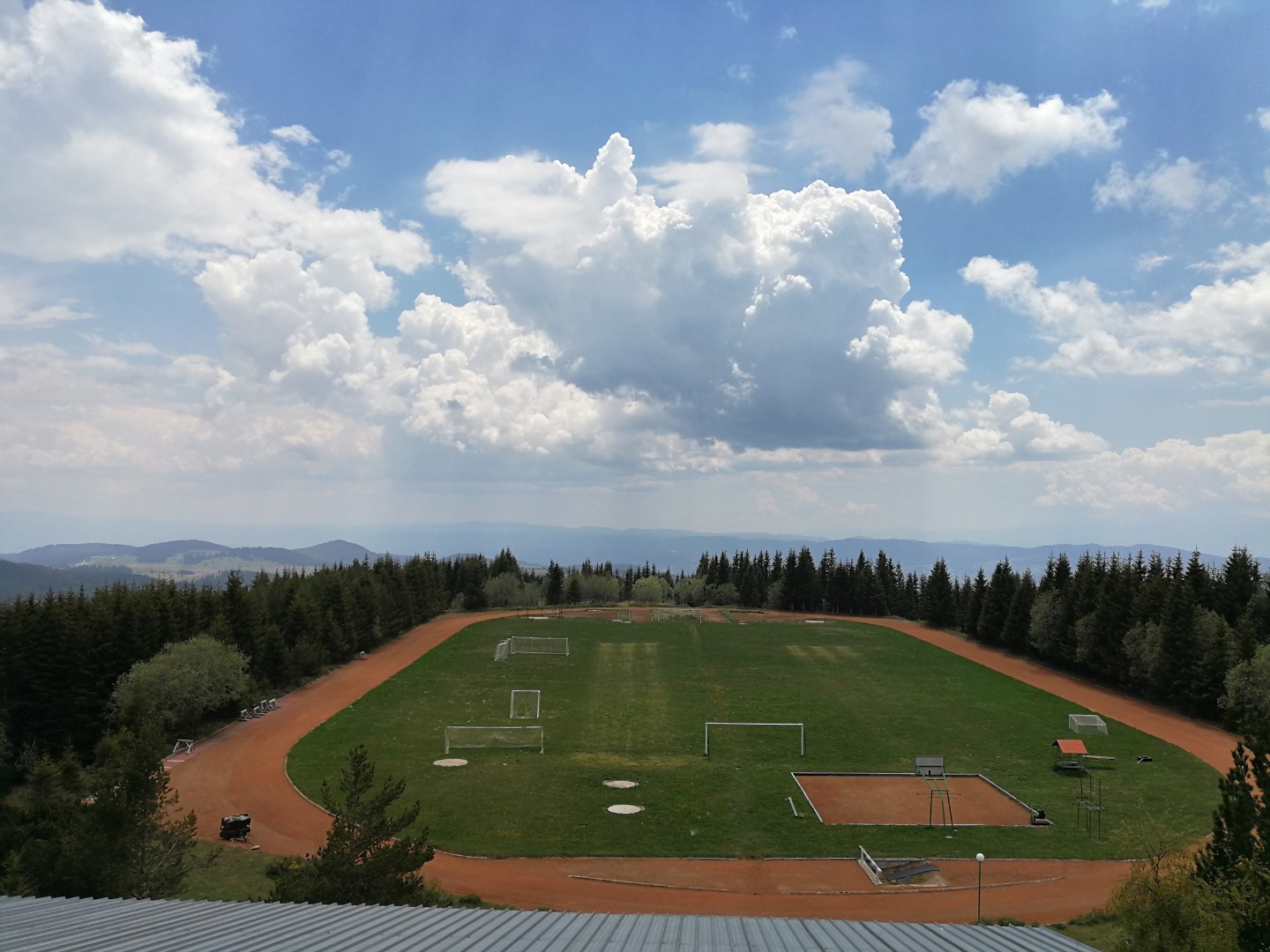 Terrain de football extérieur en gazon avec buts et piste de course, situé dans les collines pour les séances d'entraînement en stage