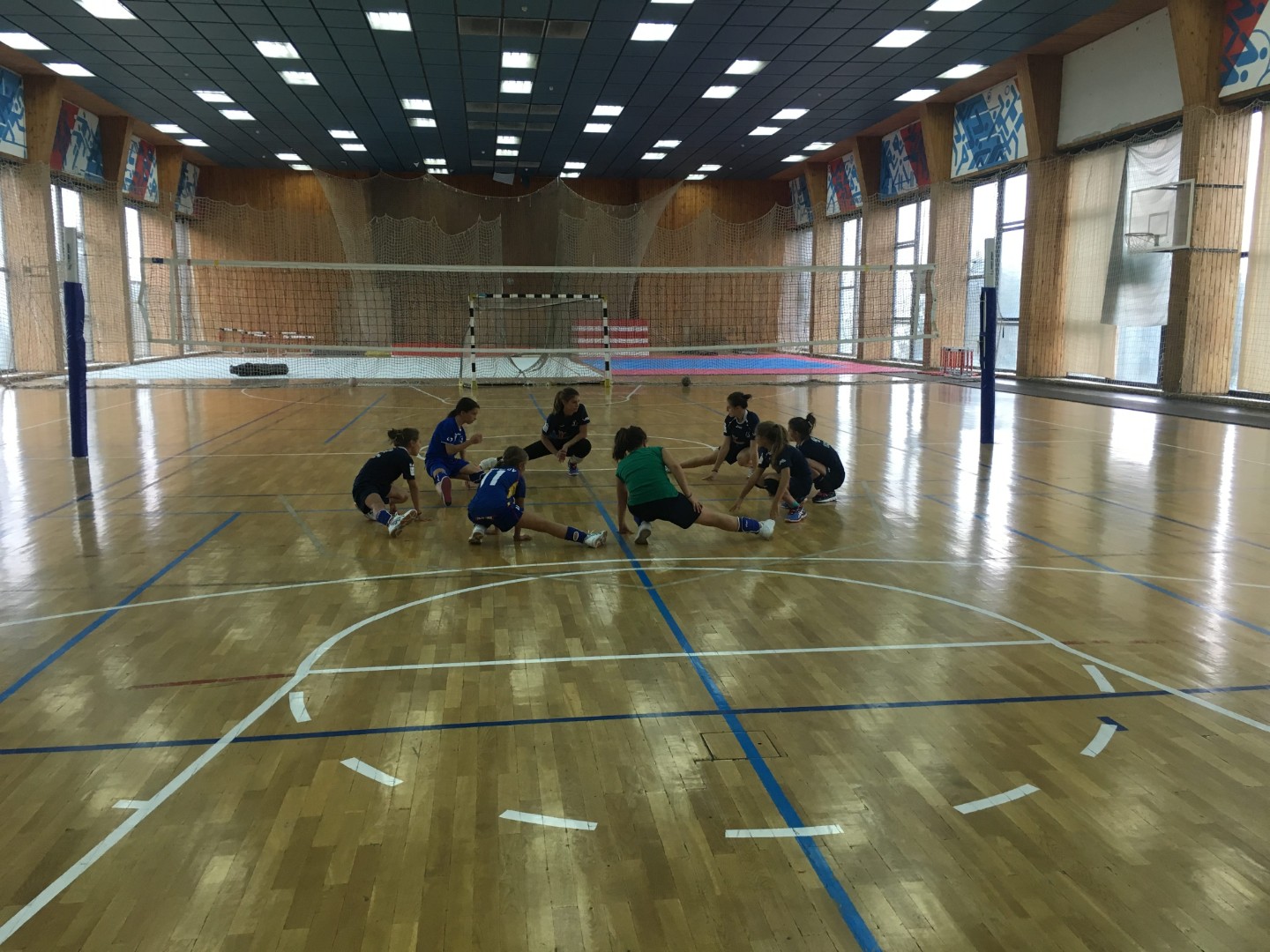 Jeunes athlètes assis en cercle sur le sol d'un gymnase, écoutant les consignes de l'entraîneur pendant un exercice en stage