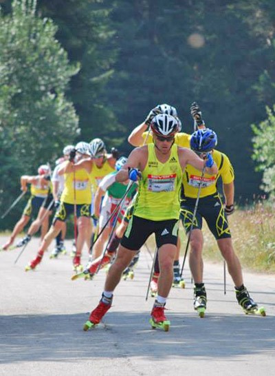 Athlètes en ski-roues montant en file indienne, portant casques et combinaisons de course pendant une séance d'entraînement
