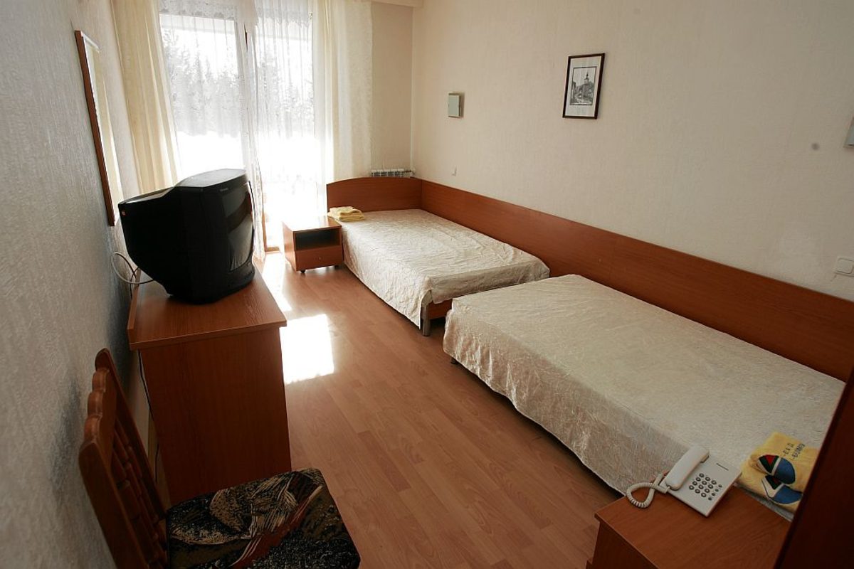 Chambre d'hôtel avec lits jumeaux, mobilier en bois, TV et lumière naturelle, hébergement des athlètes pendant le stage d'entraînement