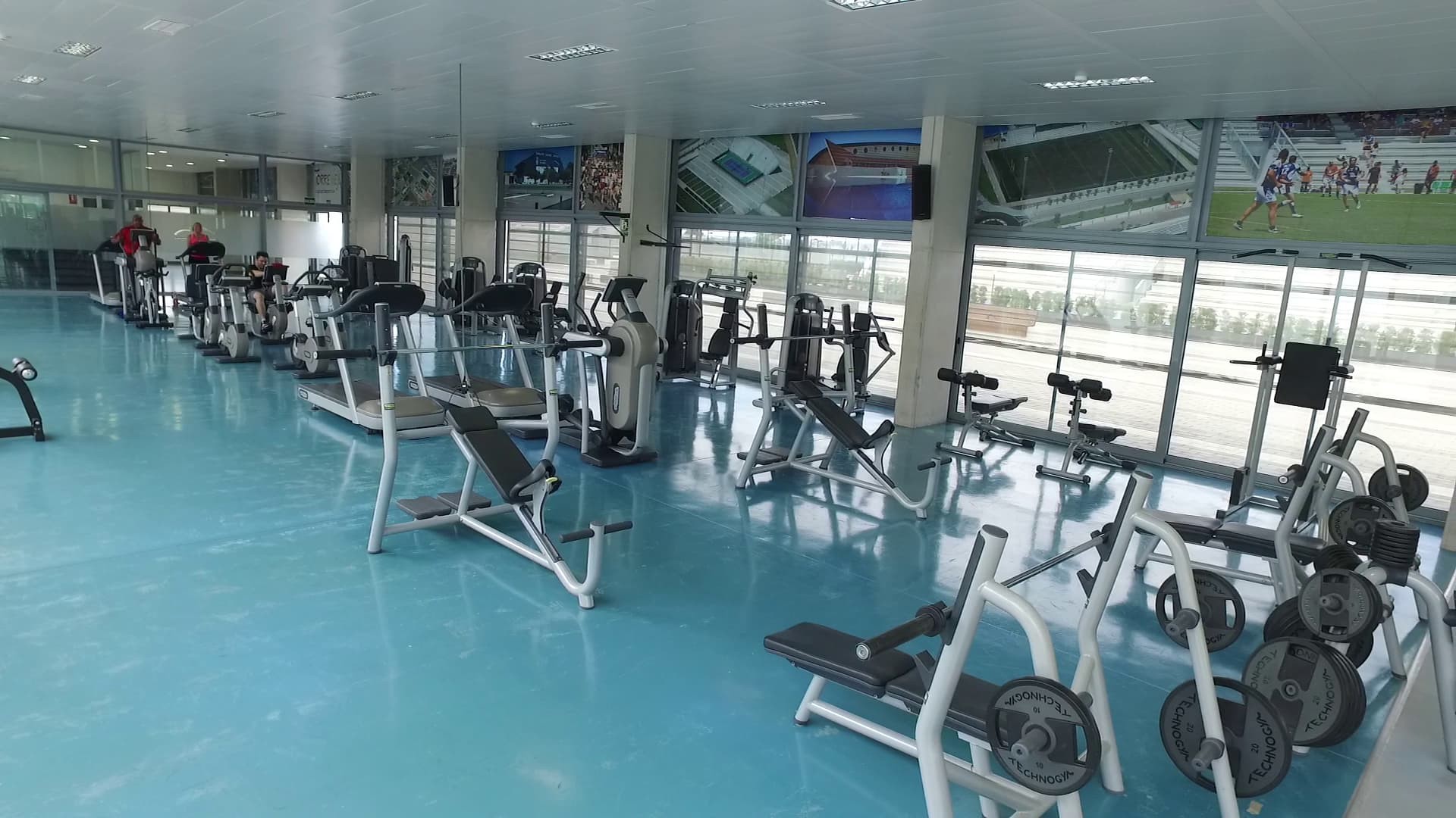 Fitnessstudio mit Cardio- und Kraftgeräten, Spiegeln und großen Fenstern.