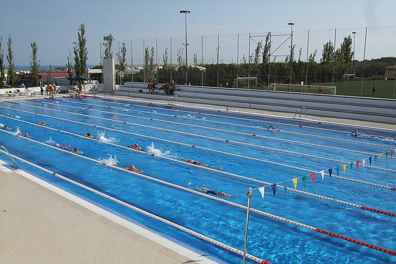 Athleten schwimmen Bahnen in einem Außenpool neben Sportplätzen.