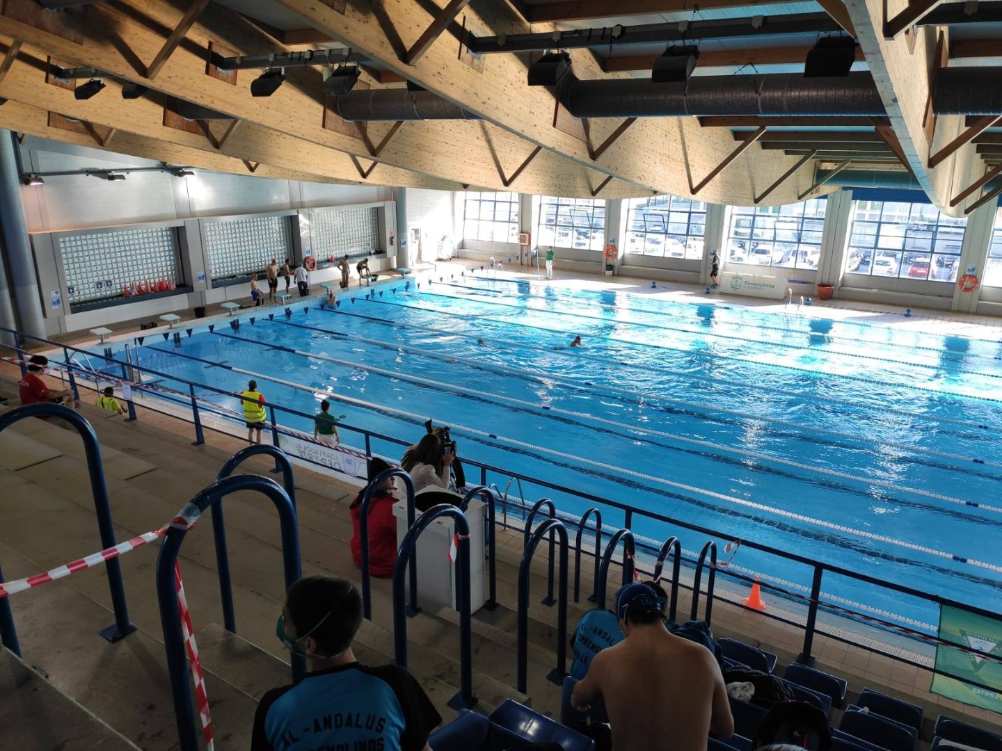 Weite Ansicht eines Hallenwettkampfbeckens mit Bahnen, Tribüne und Schwimmern im Wasser.