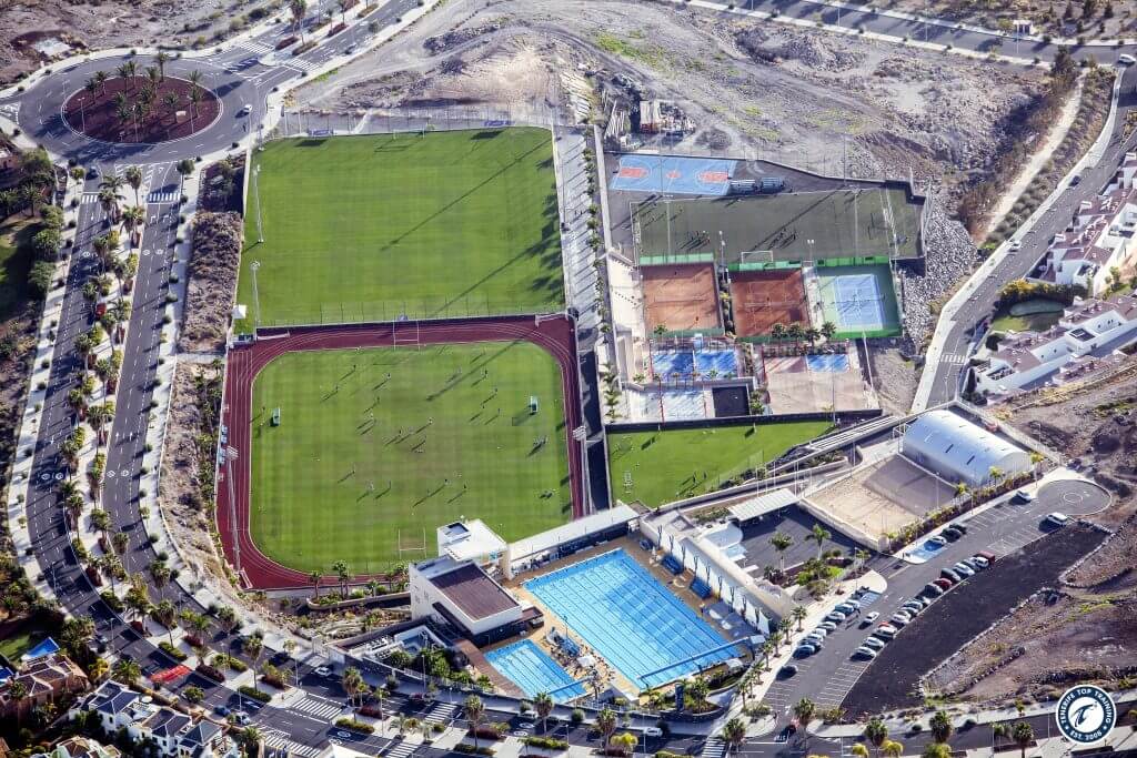 Aerial view of sports complex with football field, running track, pool and courts.